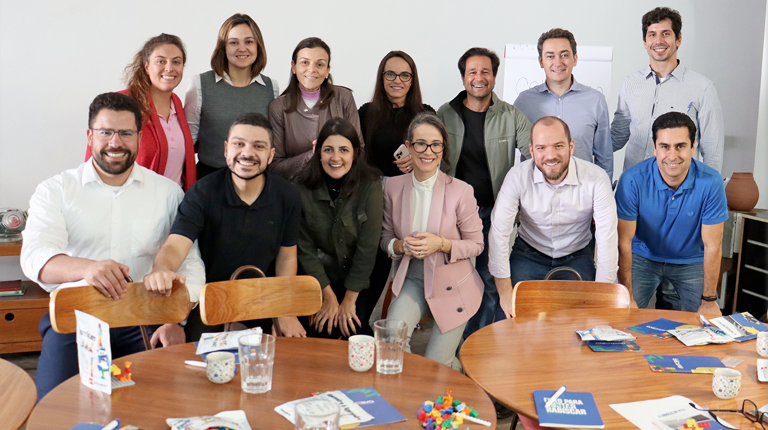 duas fileiras de pessoas atrás de uma mesa, felizes com o workshop apresentado de Liderança.