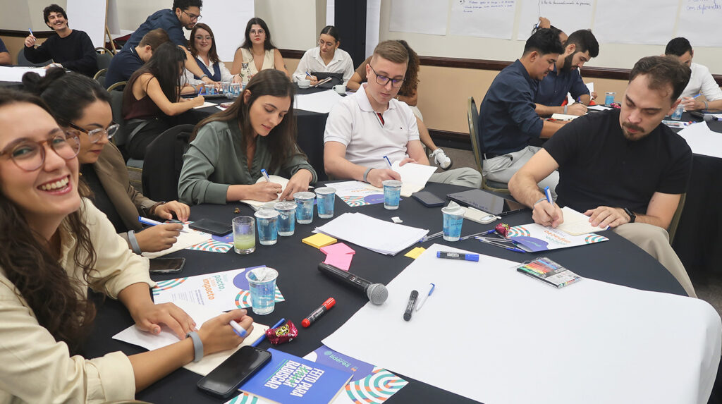 Trainees da Aegea reunidos em pequenos grupos durante exercício de narrativa corporativa.